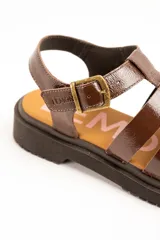 Sandalias cangrejeras de cuero marrón charol, estilo romano con múltiples tiras cruzadas, suela track plana y cierre de hebilla metálica ajustable en el tobillo.