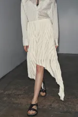 Falda midi color crudo, de tiro medio y confeccionada en viscosa. Presenta detalle de pliegues y bajo asimétrico. Cierre lateral con cremallera oculta.