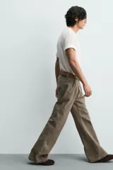 Pantalón de denim color verde oliva, estilo chino con corte ancho y bota acampanada (flare) desde la rodilla. Tiro medio, confeccionado en tejido rígido. Presenta bolsillos frontales y bolsillos traseros de plastrón.