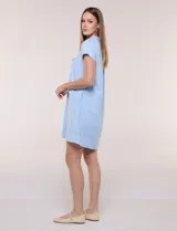 Vestido corto de lino color celeste con cuello camisero, escote en V, mangas cortas, bolsillos laterales invisibles y silueta holgada.