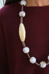 Collar largo de diseño artesanal compuesto por una cuerda central de la que cuelgan cuentas esféricas de cerámica blanca con vetas y dos piezas centrales alargadas con acabado dorado texturizado.