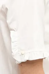 Camisa blanca de manga corta con cuello mao y detalles de volados a lo largo de la botonera frontal y en los puños.