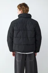 Campera acolchada de color negro con cuello alto, cierre frontal de cremallera y diseño de paneles horizontales. Cuenta con mangas largas y bolsillos laterales funcionales.