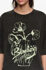 Remera oversize color blanco crudo, confeccionada en algodón, con cuello redondo y mangas cortas. Presenta un estampado frontal en color rojo de un jarrón con flores y el logo de la marca en caligrafía.