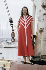 Vestido camisero midi de lino color rojo, con botones frontales, bolsillos laterales y detalles de volados rosados en forma de V en el pecho y las mangas.