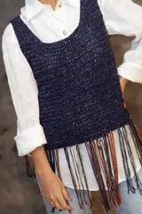 Top tejido a crochet en color dorado con destellos brillantes, de escote redondo y sin mangas. Presenta un diseño de flecos largos en la parte inferior en tonos rojo y dorado.