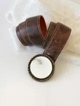 Cinto de cuero color marrón con forro de cuero y hebilla redonda con detalles de guampa. El broche es suizo, para poder usar el cuero con otras hebillas.