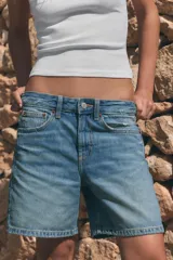 Bermuda de tiro medio confeccionada en denim de color negro gastado, con diseño de cinco bolsillos, trabillas para cinturón y cierre frontal con cremallera y botón metálico.