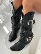 Botas de caña media color negro con efecto desgastado, diseño tipo western con múltiples correas ajustables con hebillas metálicas y detalles de ojales plateados.