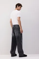 Pantalón de jean de cinco bolsillos, confeccionado en denim de algodón rígido. Modelo de corte baggy, holgado desde la cadera hasta el bajo, con piernas redondeadas extraamplias y pliegues en el tobillo. Presenta cintura clásica con cierre y tiro bajo.