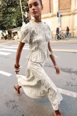 Blusa de manga corta abullonada con diseño a cuadros, cuello con volante y acabados elásticos. Cuenta con aberturas y lazos ajustables en los laterales.