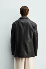 Sobrecamisa de corte relaxed fit confeccionada en tejido efecto piel de color negro, con cuello solapa, manga larga, bolsillos con solapa en la cadera y cierre frontal de botonadura.