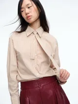 Camisa de corte clásico con estampado de rayas verticales en tonos beige y blanco. Presenta cuello camisero, cierre frontal con botones y corbata integrada del mismo tejido y estampado.