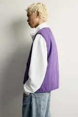 Chaleco acolchado de algodón color violeta con efecto lavado, cuello en V, cierre frontal con cremallera y bolsillos de plastrón delanteros.