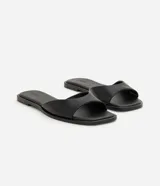 Sandalia mule plana de cuero color negro, con diseño minimalista, capellada ancha y punta cuadrada.