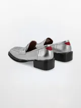 Mocasín plateado de cuero con punta cuadrada, detalle de estrella y talón en rojo.