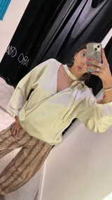Blusa de satén color beige, con diseño reversible que permite usar el escote pronunciado hacia el frente o hacia la espalda. Presenta mangas largas abullonadas con puños elásticos y un lazo integrado en el cuello para anudar.