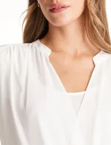 Blusa de gasa blanca, marca Catherine Malandrino, con cuello a la base y escote en V pronunciado. Incluye una pieza interna a tono para un escote discreto. Tiene manga larga con puño ancho y botón.