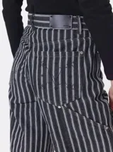 Pantalón de tiro medio y pierna ancha confeccionado en denim de algodón grueso. Presenta un diseño a rayas verticales en tonos azul y celeste, con costuras en contraste color rojo, bolsillos laterales tipo cargo y remaches metálicos.