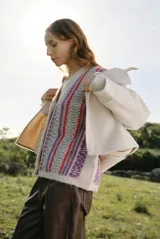 Cardigan de punto con escote en V y cierre frontal de botones. Presenta un diseño estampado con patrones geométricos en tonos beige, marrón y detalles en azul vibrante.