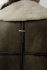 Chaleco de piel sintética en color chocolate, con cierre frontal y detalles de cuero en los bordes. Presenta un diseño de cuello solapa y ajuste lateral con hebillas.