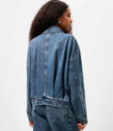 Campera de jean azul con pliegues frontales y posteriores, cuello clásico, cierre frontal embutido y mangas largas. Presenta un diseño de silueta levemente ajustada con terminaciones simples en puños y bajo.