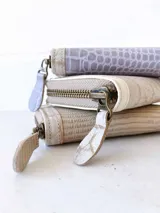 Billetera pequeña con cierre metálico, cuerpo principal de cuero lila texturizado y ribetes en color crema. Presenta un parche de cuero marrón con la palabra "chowie" escrita en cursiva.