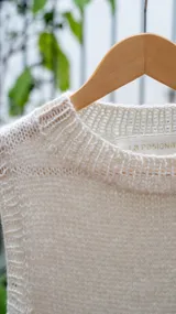 Chaleco tejido de punto en color crudo, con cuello alto y diseño sin mangas. Presenta una textura de punto grueso y corte recto.