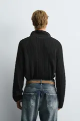 Polo de punto negro con diseño de estructura abierta, cuello solapa y cierre frontal ajustable mediante cordones. Presenta mangas largas y terminaciones en rib.