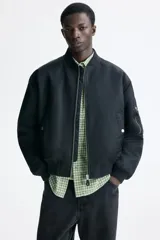 Campera bomber de nylon color negro, con cuello, puños y bajo acanalados. Presenta cierre frontal, bolsillos laterales con botón a presión y un bolsillo con cierre en la manga.
