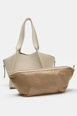 Bolso formato shopper de color beige, con detalle de pespuntes, cremalleras laterales con tiradores, doble asa y compartimento interior extraíble con cierre imantado.