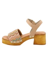 Sandalia de estilo sueco con plataforma y taco cuadrado de madera. Presenta una banda frontal tejida en rafia multicolor con detalles de tachas metálicas y una tira de sujeción al tobillo en cuero color nude con cierre de hebilla.