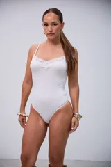 Body blanco elastizado con tirantes finos y escote en V decorado con encaje floral y un pequeño lazo.