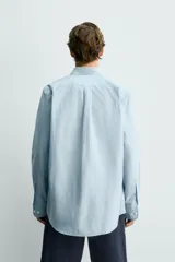 Camisa de corte relajado color celeste, confeccionada en mezcla de algodón y seda. Presenta cuello solapa, cierre frontal de botones, manga larga con puños abotonados y dos bolsillos de plastrón con solapa en el pecho.