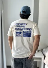 Remera beige de manga corta con estampado gráfico en azul en la espalda que incluye el texto "BROKERS GRAPHIC RESEARCHING" y "THE NEW WAVE BROKERS".