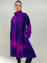 Tapado de lana merino afieltrada con diseño artesanal teñido en tonos violeta y fucsia. Presenta cuello elevado, cierre frontal con broches ocultos, bolsillos laterales y un corte ligeramente más largo en la parte trasera.