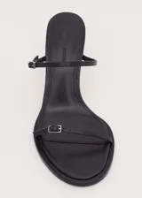 Sandalias de tacón alto color negro, con diseño minimalista de tiras finas cruzadas en el empeine y cierre con hebilla en el tobillo.