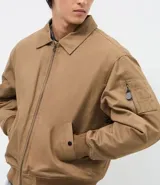 Campera bomber de sarga color tostado con cuello desmontable de pelo sintético oscuro. Presenta cierre frontal de cremallera, puños y cintura acanalados, y bolsillos laterales.