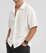 Camisa de manga corta color blanco, de corte holgado y tejido texturizado con cierre frontal de botones.