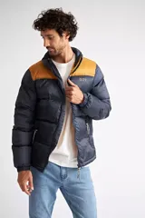Campera puffer de nylon para hombre, con diseño bicolor en azul marino y mostaza en la parte superior. Cuenta con cierre frontal completo, mangas largas con puños elásticos y bolsillos laterales con cierre. Incluye logo estampado en el pecho.