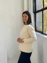 Sweater de punto color beige, con cuello redondo, manga larga y dos bolsillos frontales tipo parche.