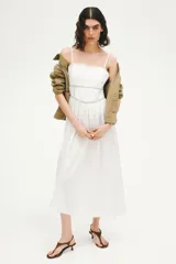 Vestido midi de algodón color blanco, con escote halter y breteles para atar en la nuca. Presenta detalles de encaje en el escote y la cintura, y falda fruncida con leve vuelo.