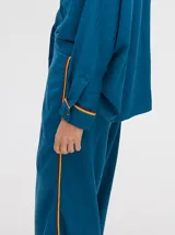 Pantalón de corte holgado y tiro alto con caída recta, color azul petróleo. Presenta una franja lateral decorativa en tonos rojo y amarillo que recorre la pierna, a juego con la camisa de la misma línea.