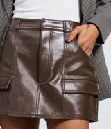 Short pollera de tiro medio confeccionado en poliuretano con acabado brillante. Presenta diseño de corte recto con bolsillos frontales tipo cargo con solapa y cierre frontal con cremallera.