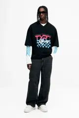 Remera de malla negra con cuello en V, mangas cortas y hombros caídos. Presenta un estampado frontal con la frase "THUNDER X RACING TEAM" y un diseño gráfico en tonos rosa, azul y celeste con la palabra "RACING" y un patrón de cuadros.