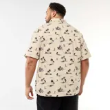 Camisa de manga corta color beige con estampado tropical de palmeras y veleros en tonos oscuros, cuello cubano y un bolsillo aplicado en el pecho.