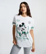 Remera blanca de algodón con cuello redondo y mangas cortas. Presenta un estampado frontal de Mickey Mouse con temática de tenis y detalles de rayas verdes en las mangas.