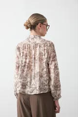 Camisa de manga larga con cuello con volados y botones nacarados. Presenta un estampado romántico de inspiración barroca en tonos azul y beige.