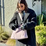 Bolso tipo tote color gris claro, con doble asa de mano y correa larga regulable. Tiene dos bolsillos laterales y un bolsillo frontal.