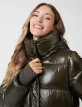 Campera puffer larga de abrigo marca BCBG Maxazria, color beige. Cuenta con capucha desmontable, cuello alto envolvente, cierre frontal bidireccional con solapa de botones a presión, bolsillos laterales, puños internos elastizados y tajos laterales con cierre en el bajo.